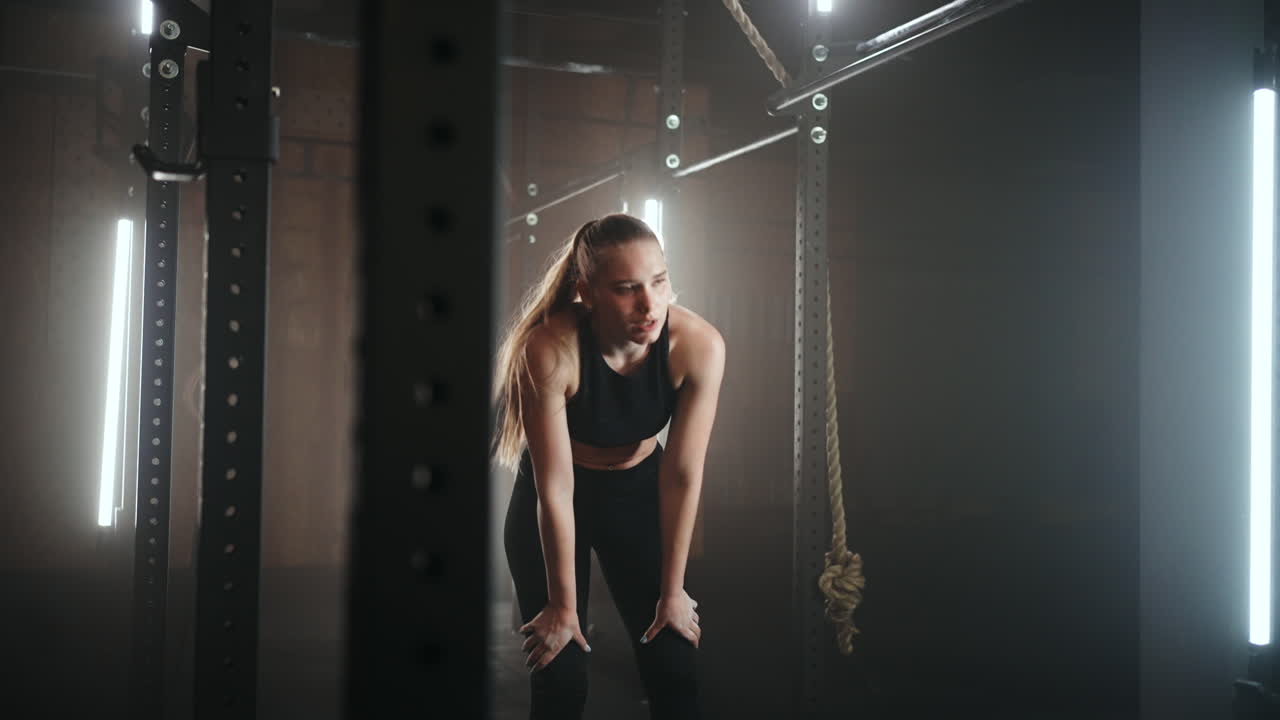 A sporty young woman pulls herself up on a horizontal bar in a dark gym in a beautiful neon backlight. Endurance and perseverance in pulling up movement towards the goal