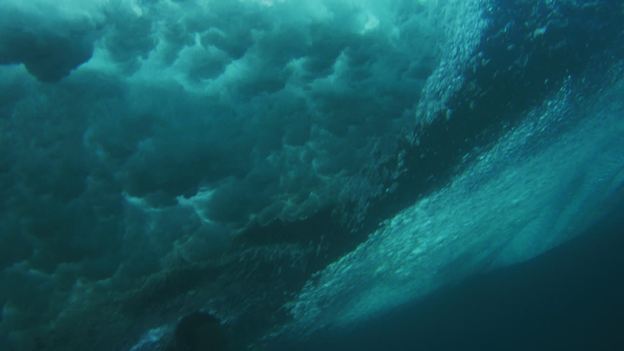 Water sprays misting surface of wave as surfer duck dives under