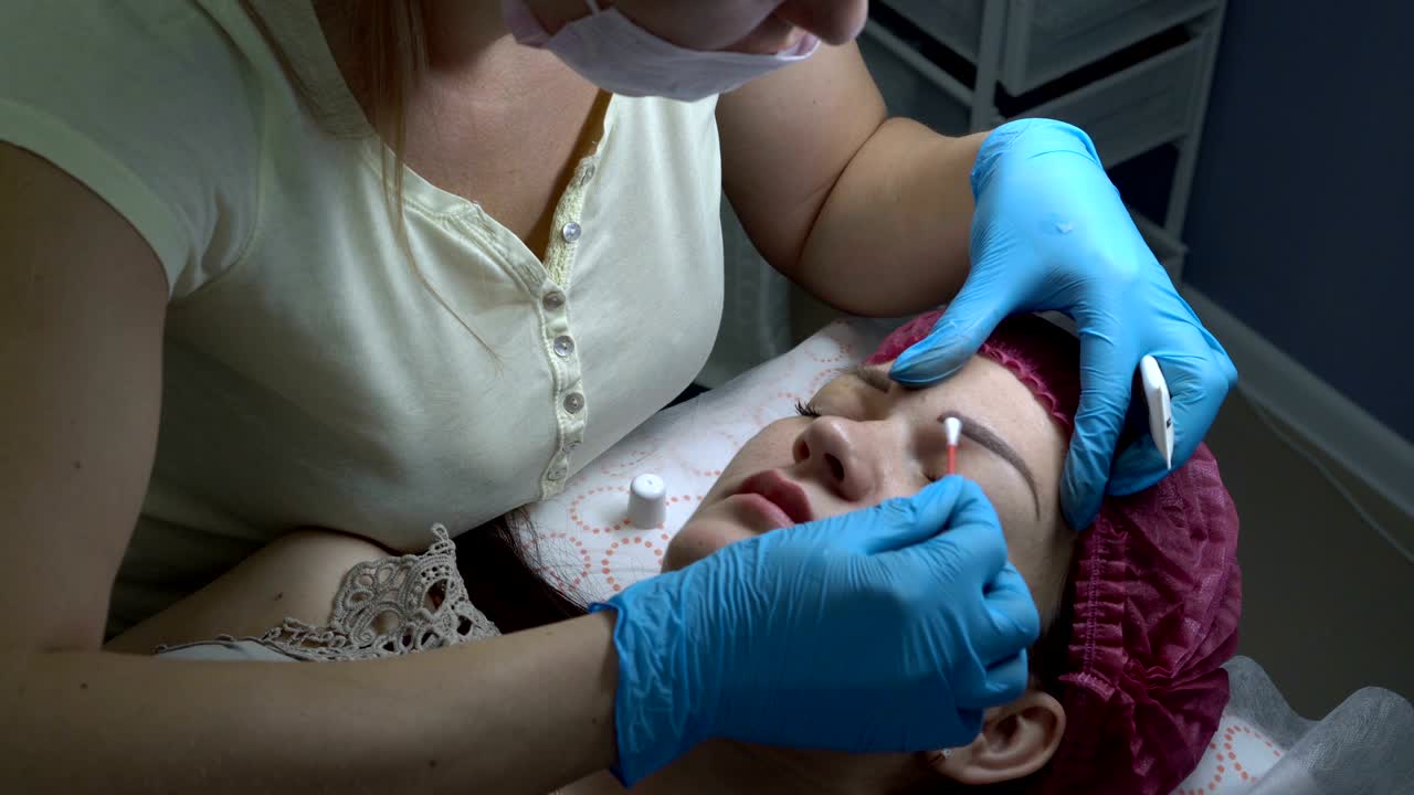 A woman-cosmetologist smears the cream of the eyebrows of a young girl after a microblading procedure in a beauty salon. Permanent makeup eyebrows.