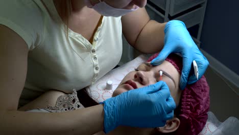 una mujer-cosmetóloga frota la crema de las cejas de una chica joven después de un procedimiento de microblading en un salón de belleza. cejas de maquillaje permanente.