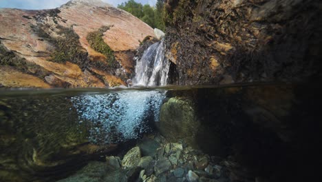 A-picturesque-scenery-of-a-shallow-river-with-rocky-shores,-crystal-clear-water,-and-a-tiny-waterfall