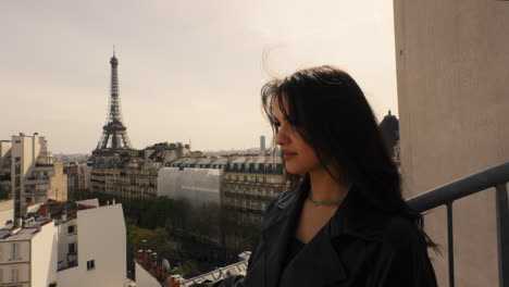 beautiful young brunette woman standing on a rooftop with the famous tour eiffel in the background, in paris, france