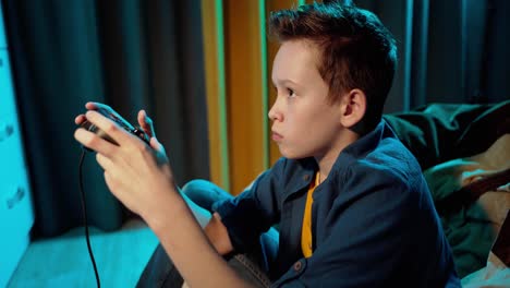 concentrated boy playing video games in his room. side view of a young teenage boy holding joystick and playing at home.