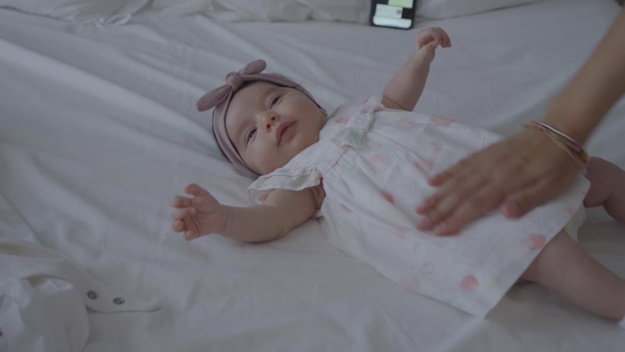Adorabile neonato sdraiato su un grande letto bianco, accarezzato e vestito dalla sua amorevole madre.