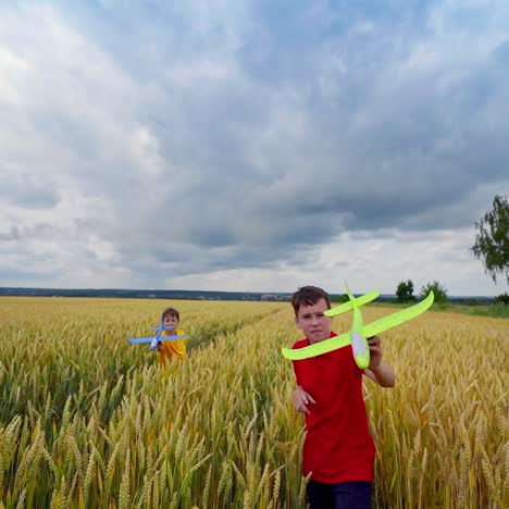 children playing in farmland. boys running with toy planes in the wheat field in summer. brothers having fun outdoors under cloudy sky. front view.