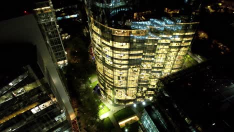 aerial view establishing an office building illuminated at night, modern glass building, nueva las condes santiago chile