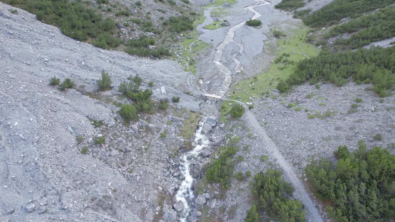 imágenes aéreas de drones que vuelan a lo largo de un río y se inclinan lentamente para revelar un espectacular valle glacial rodeado de montañas escarpadas y pinos con parches de nieve en suiza