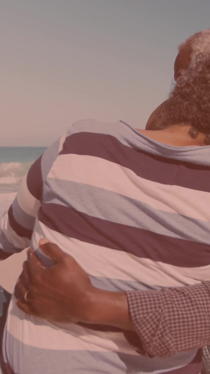 Vista posteriore di una coppia afroamericana che si abbraccia mentre è seduta in spiaggia