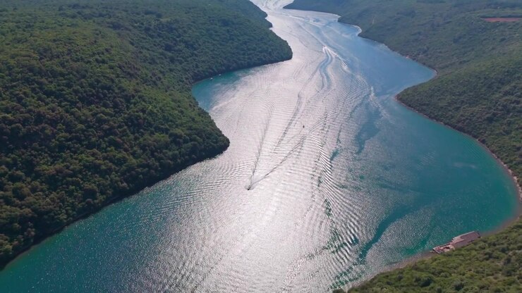 Vista drone sul Canale di Leme verso l'ingresso dell'Adriatico aperto, con acqua luminosa e soleggiata, barche e pendii boscosi che circondano la baia simile a un fiordo. Istria, Croazia.