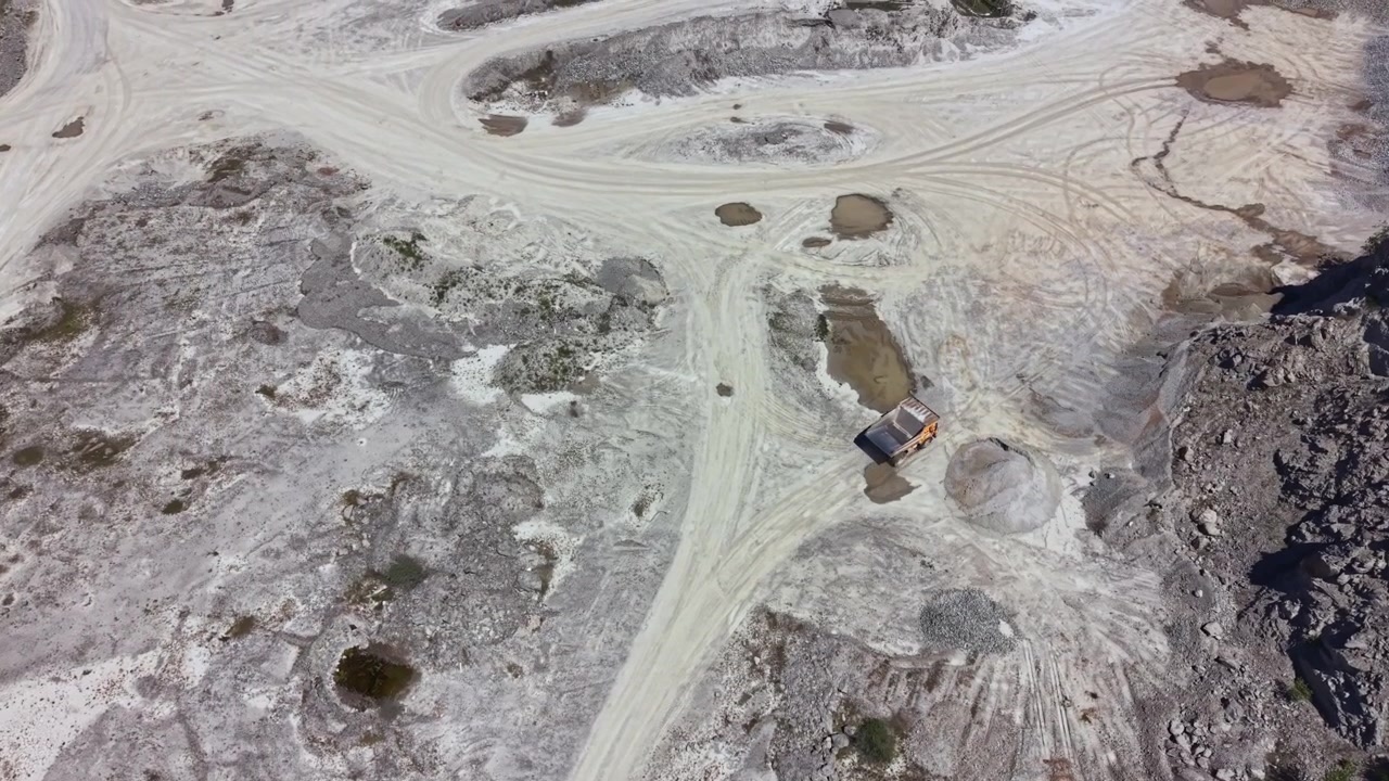 Truck moves along the dusty road in a quarry in the afternoon sun while workers prepare equipment in the background for mining stone