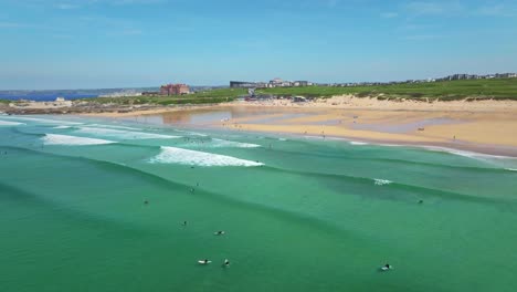 Fistral-Beach-Scenery-with-Turquoise-Waters,-Ocean-Waves-and-Surfers-Enjoying-the-Cornish-Summer,-UK