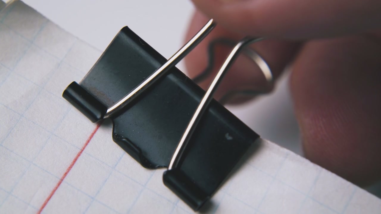 person fixes metal clamp on paper sheets on white background