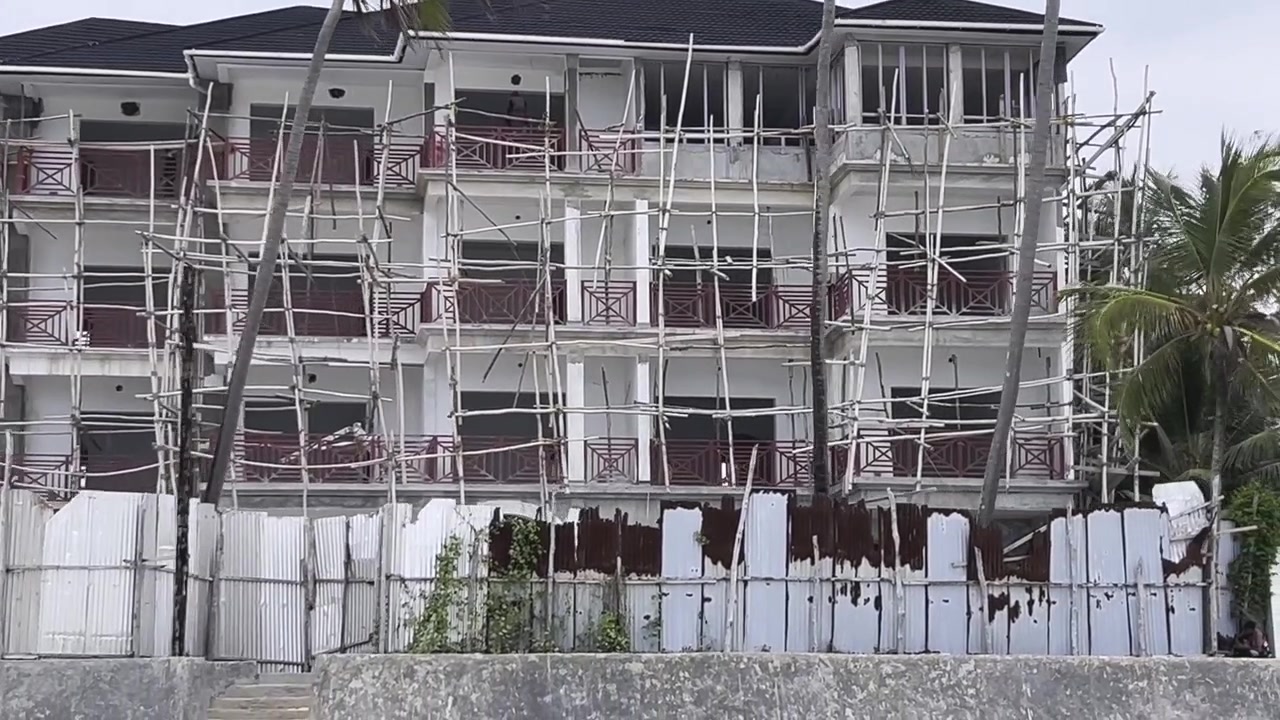 Grande edificio in costruzione con impalcature di legno non sicure che non rispettano gli standard di sicurezza di base, evidenziando condizioni di lavoro pericolose a Zanzibar, Tanzania.