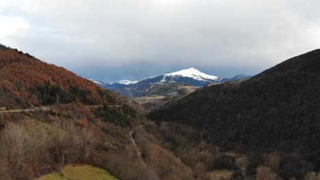 aerial: valley with a road with little traffic and a train track in a mountainous landscape with snow covered mountains in the background