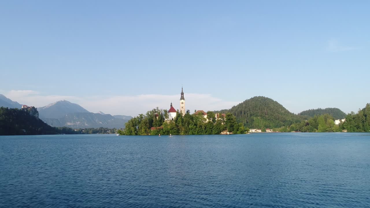 Chiesa sull'isola del Lago di Bled, ripresa aerea con drone sopra l'acqua blu, persone che remano, Alpi Giulie, destinazione turistica estiva europea