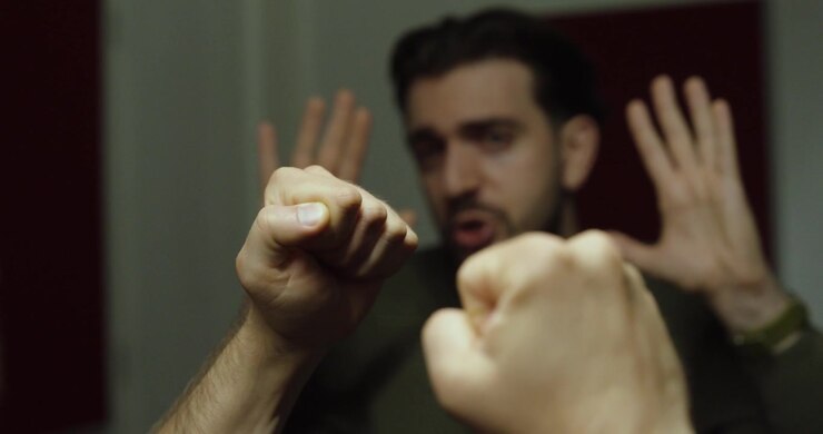 Persona che alza i pugni in modo minaccioso durante un confronto teso, mentre l'altra persona reagisce difensivamente. Adatto per conflitto, intimidazione, aggressione, bullismo, autodifesa