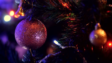 bola de navidad con brillo colgando de un árbol de navidad en un fondo oscuro de agujas verdes con guirnaldas parpadeantes. primer plano de la decoración de navidad rosa