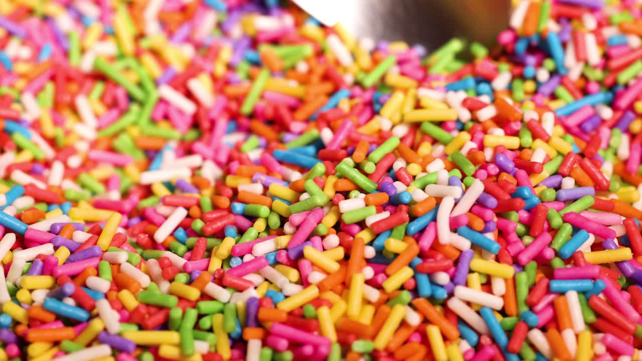 A spoon scoops vibrant sprinkles from a pile
