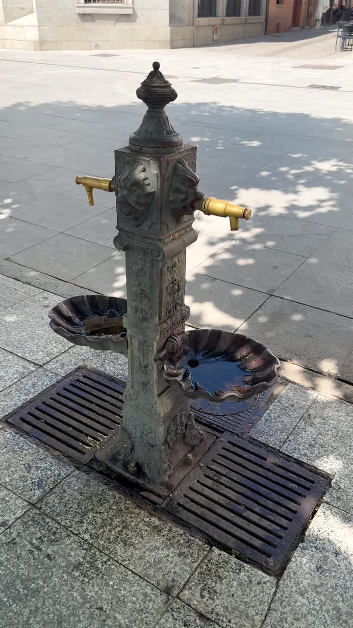 Tourist drinks from street fountain in Madrid, enjoying sunny day