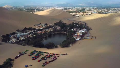 Antenne,-Rückzug,-Drohnenschuss,-Der-An-Einem-Sonnigen-Tag-In-Südperu-Von-Der-Huacachina-Oase-Und-Dem-Dorf-Wegsteigt