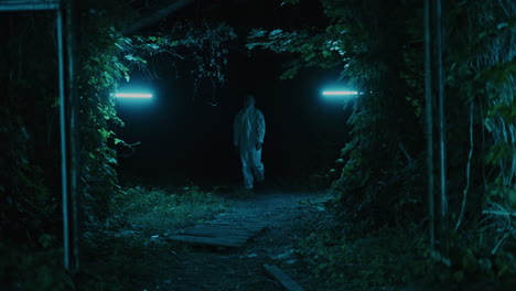 a person in protective gear walks through a dark forest at night