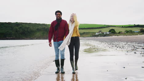 loving couple walking arm in arm along beach shoreline on winter vacation