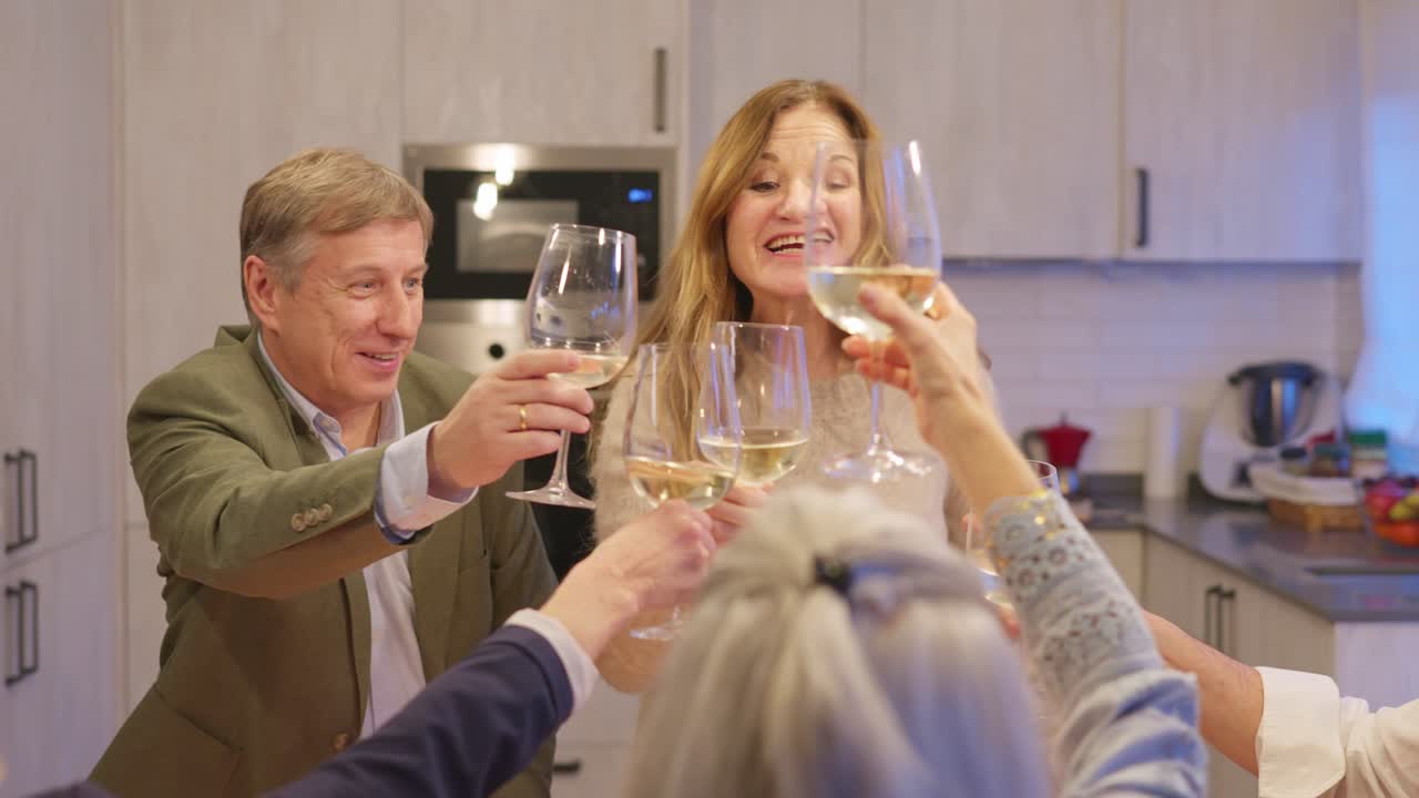 Happy Group of Friends Making a Toast with White Wine in a Modern Kitchen