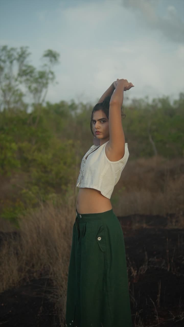 Indian woman in loose attire stretches with raised arms in early morning light amid dry grassland. India