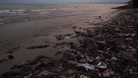 High-angle-gimbal-shot-of-beach-with-lot-of-garbage-in-sand,-sunset