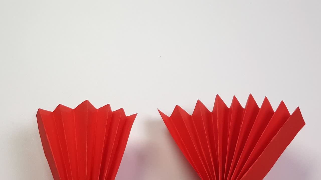Colored origami paper looks like a red fan on a white background. Chinese New Year holiday background, creativity, top view, 4K video