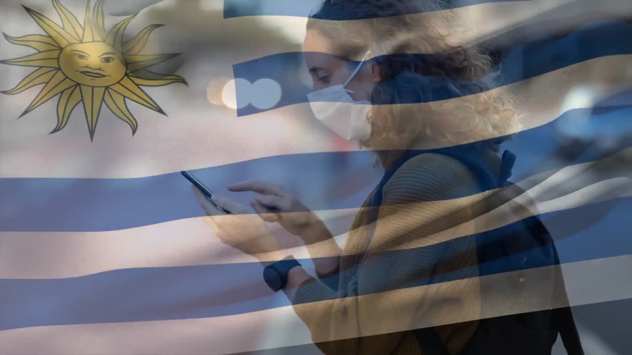 우루과이 국기가 스마트폰을 사용하는 얼굴 마스크를 쓰고 있는 여성을 향해 흔들리고 있습니다.