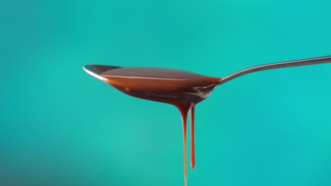 close up of melted chocolate dripping from overflowing spoon against blue coloured background with copy space