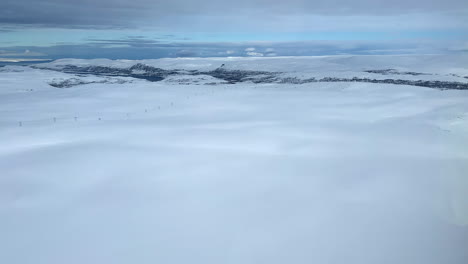 Aerial-view-of-a-snow-covered-National-park-in-Finnmark,-Northern-Norway,-Power-lines-going-over-the-mountain