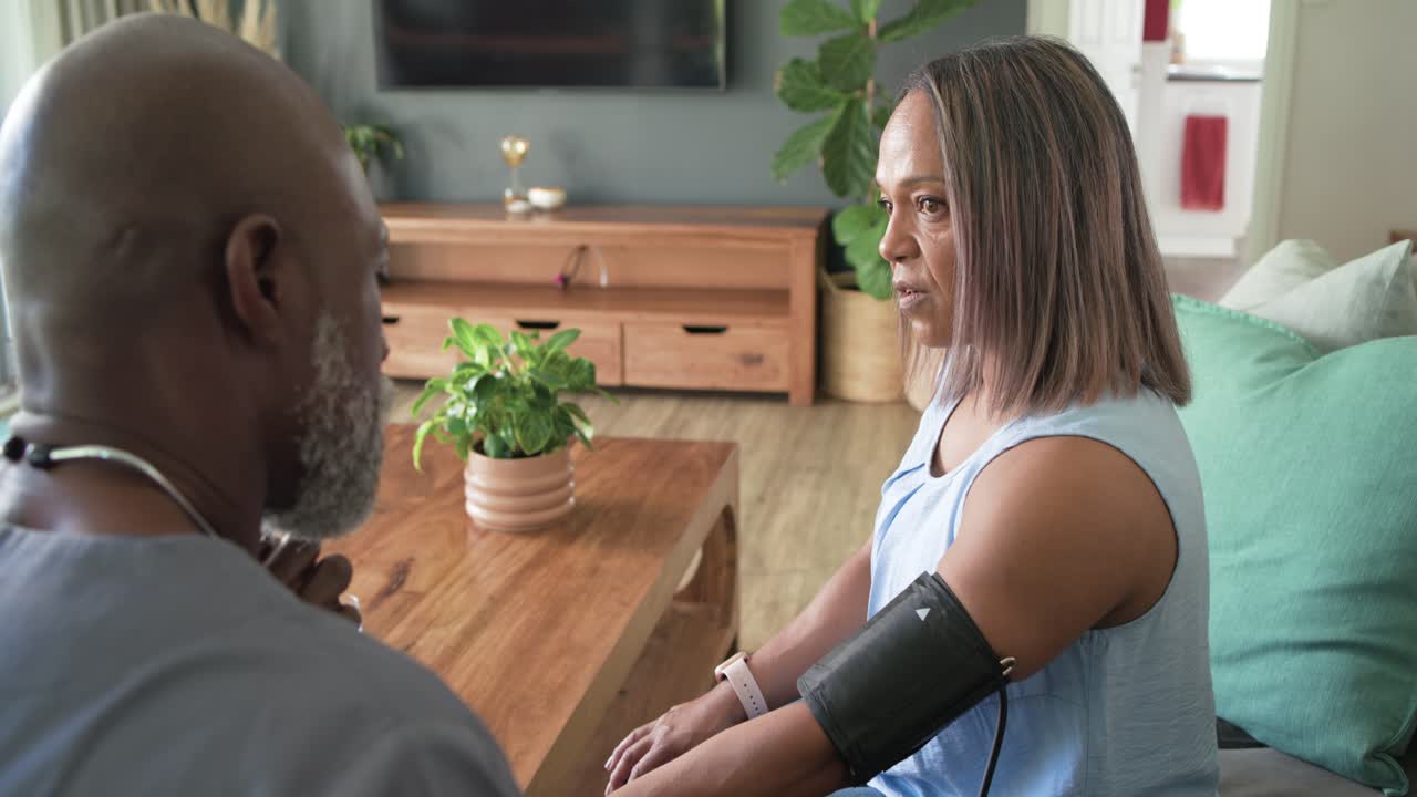 Senior couple at home African American man approaching, placing cuff and checking blood pressure
