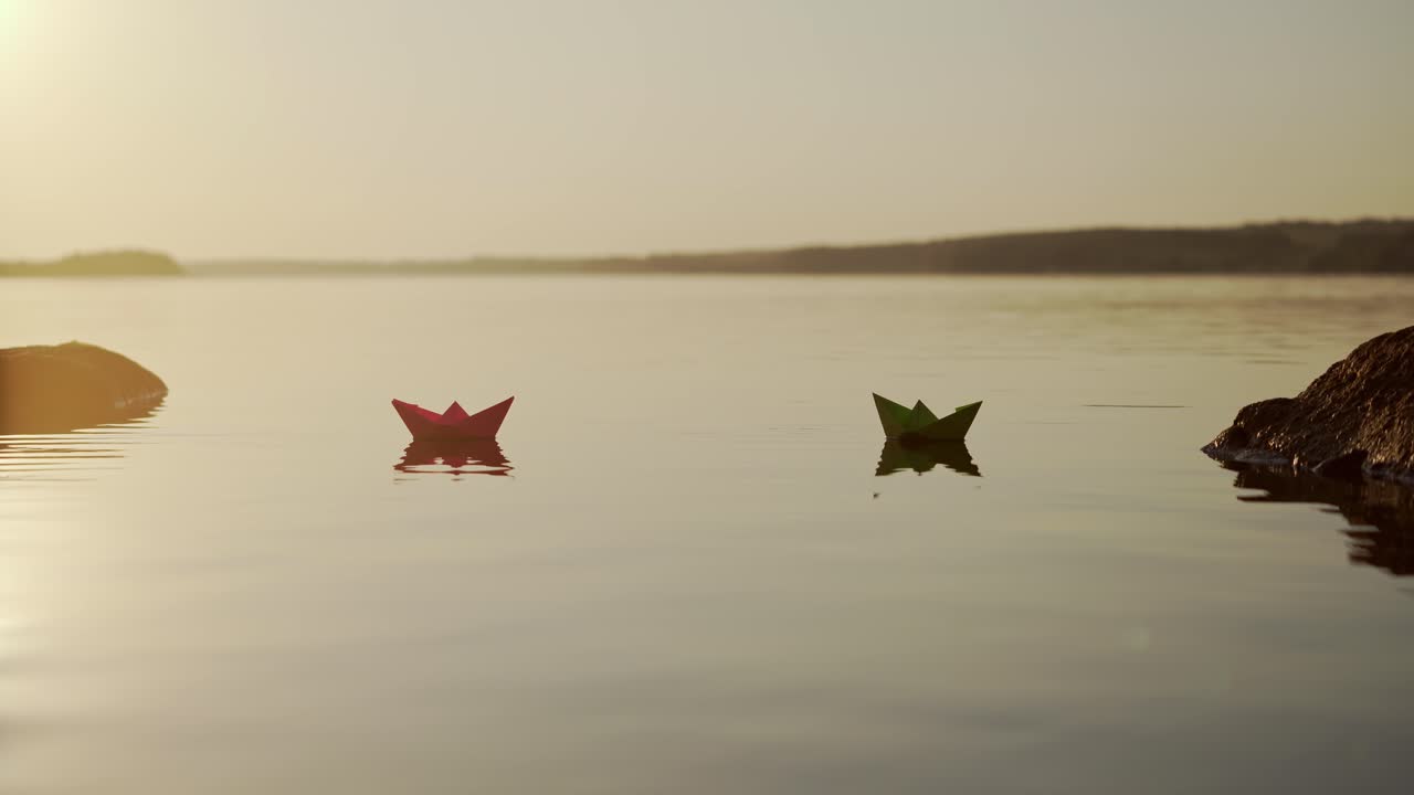 Paper boats on water at sunset. Nice homemade ships floating near the stones on the evening lake. Freedom and hope concept.