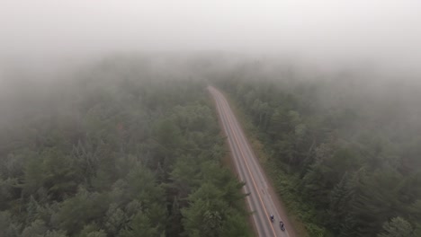 drone following 2 motorcyclists winding through northern ontario forest through cloud cover