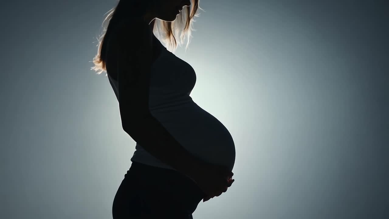 Silhouette of a pregnant woman gently caressing her belly against a soft gray background, embodying motherhood and love