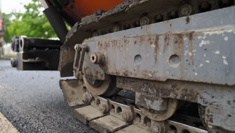 Asphalt-tracked-paver-slowly-moving-on-freshly-made-road---close-up