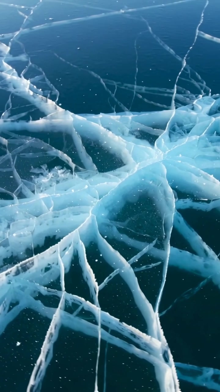 Video verticale: Inizia una lenta panoramica, con un drone che si muove sopra un lago ghiacciato, rivelando crepe nel ghiaccio con bordi bianchi