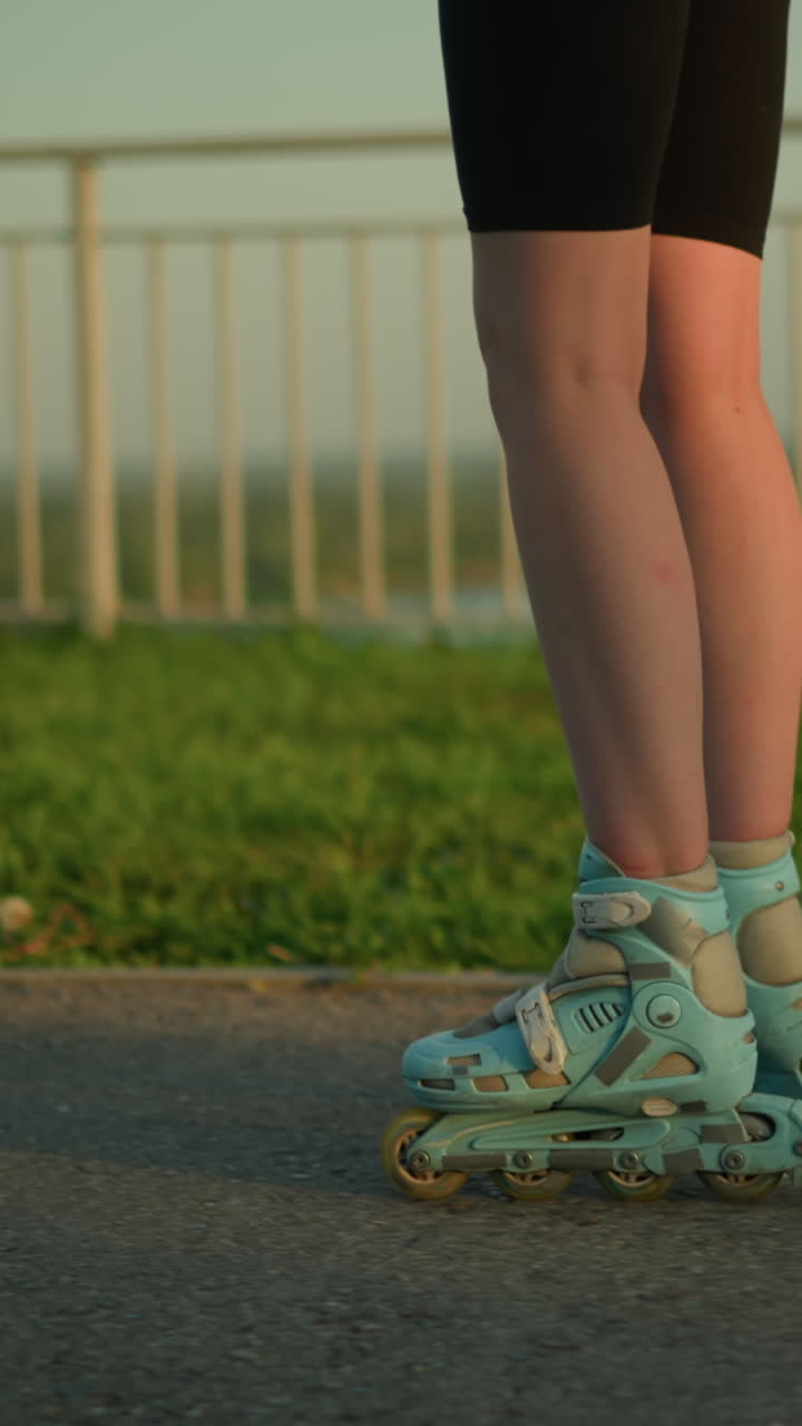 Leg view of person roller skating skillfully outdoors near iron railing, with rollerblades gliding on path and blurred cityscape in background featuring greenery and softly lit buildings