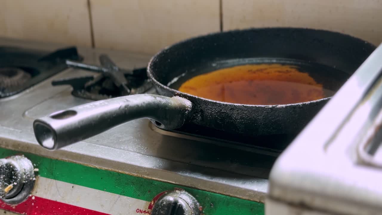 Primo piano di una padella in ghisa con salsa arancione bollente che sobbolle su un vecchio fornello a gas rustico, scattato in interni in un'ambientazione di cucina tradizionale.