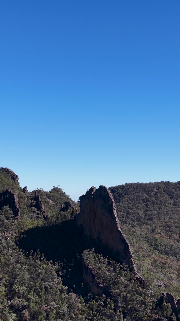 Ampia inquadratura statica della formazione rocciosa Breadknife sotto un cielo azzurro limpido nel Parco Nazionale di Warrumbungle.