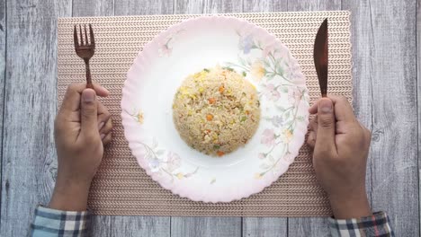 joven con un tenedor esperando en un plato lleno de arroz
