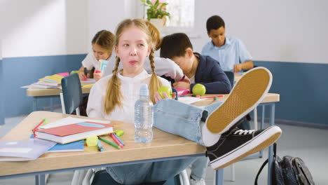 female student sitting at the desk with her legs on the table in english classroom while eating an apple