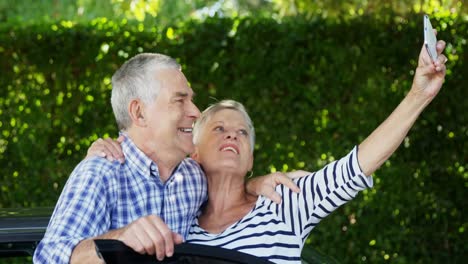 Senior-couple-taking-a-selfie-on-mobile-phone-near-car