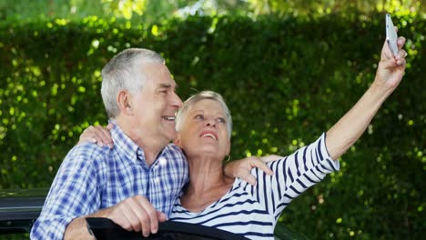 pareja de ancianos tomando un selfie en el teléfono móvil cerca del coche