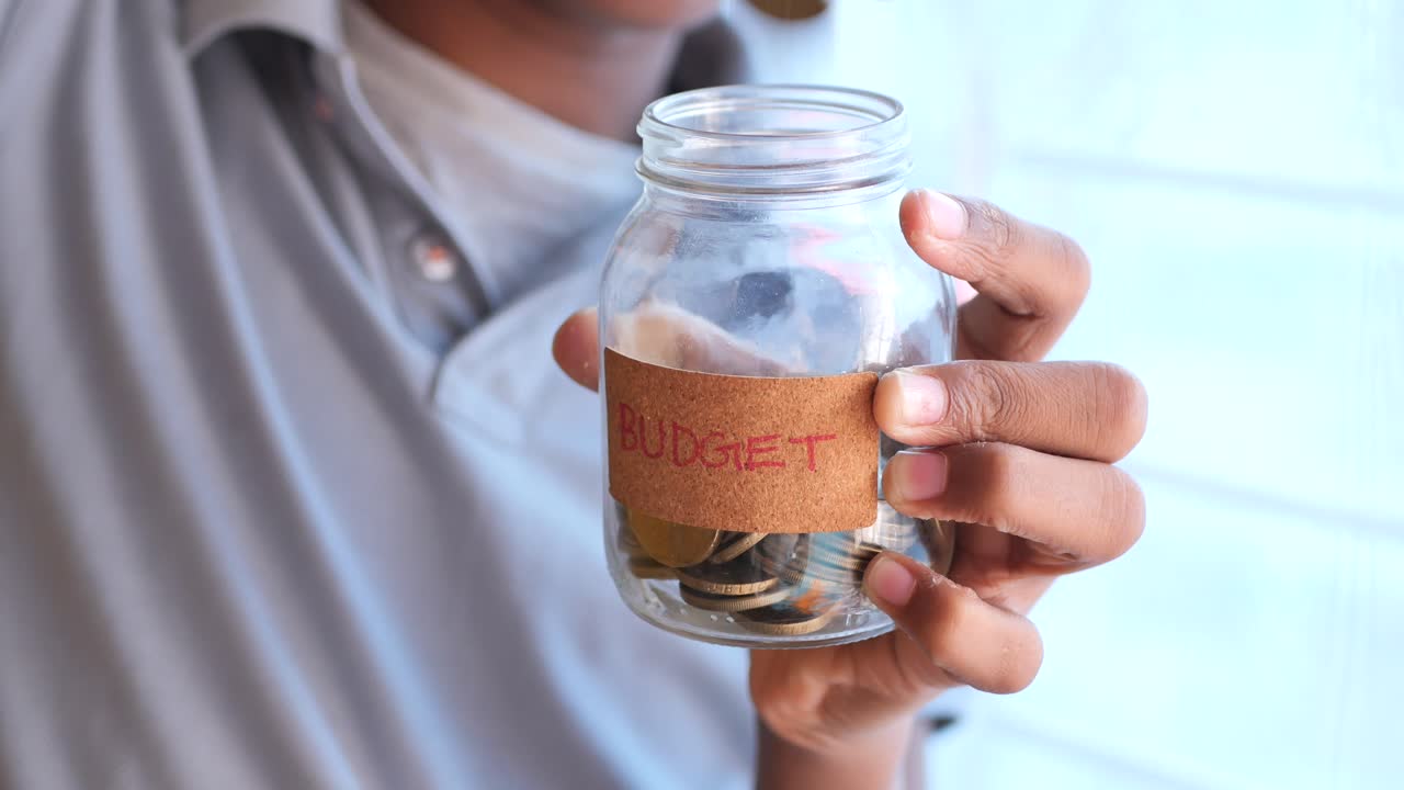 Child holding a glass jar with coins labeled "budget"