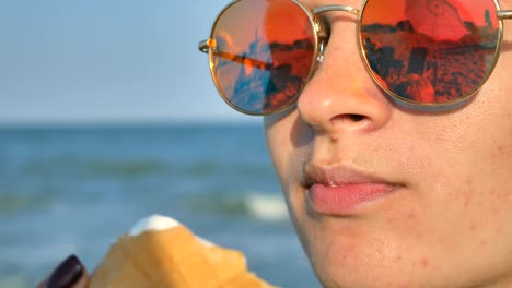 young brunette woman licking eating icecream on the beach, blue sea background and sunglasses.