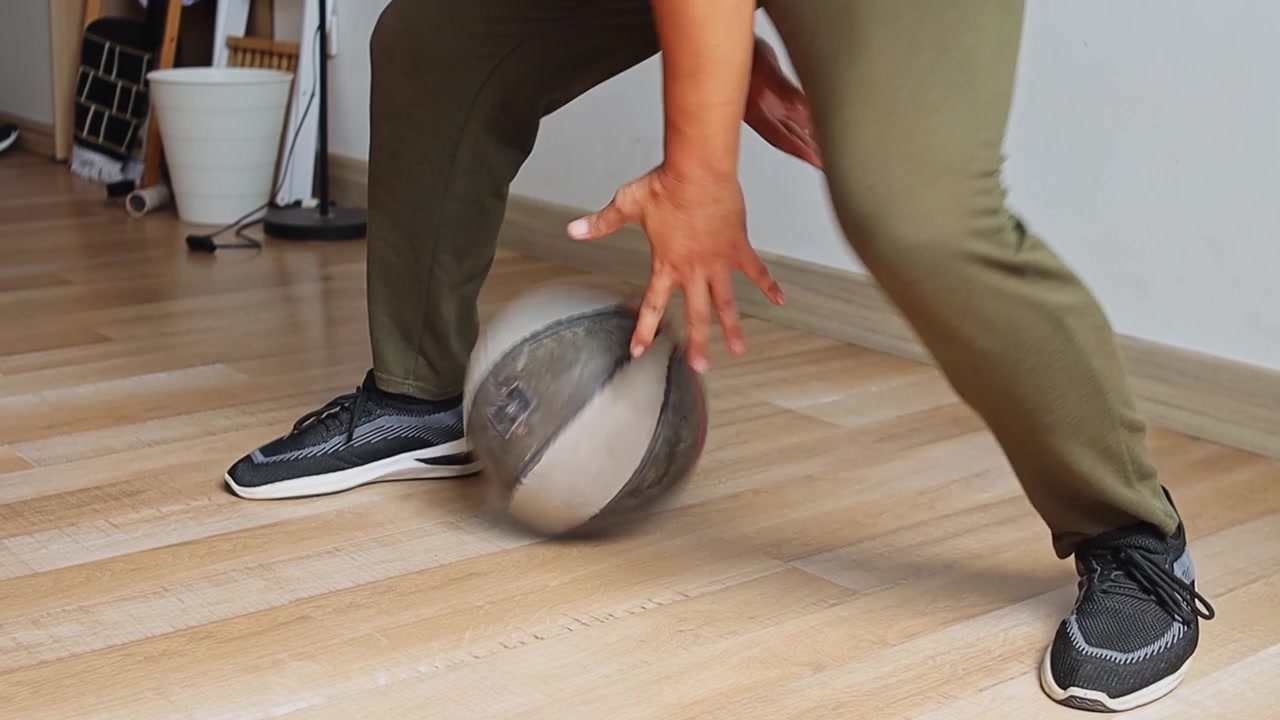 Close-up on legs and feet as player dribbles basketball between legs on wood flooring