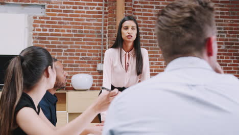 Joven-Empresaria-De-Pie-Y-Liderando-La-Reunión-De-Oficina-Alrededor-De-La-Mesa